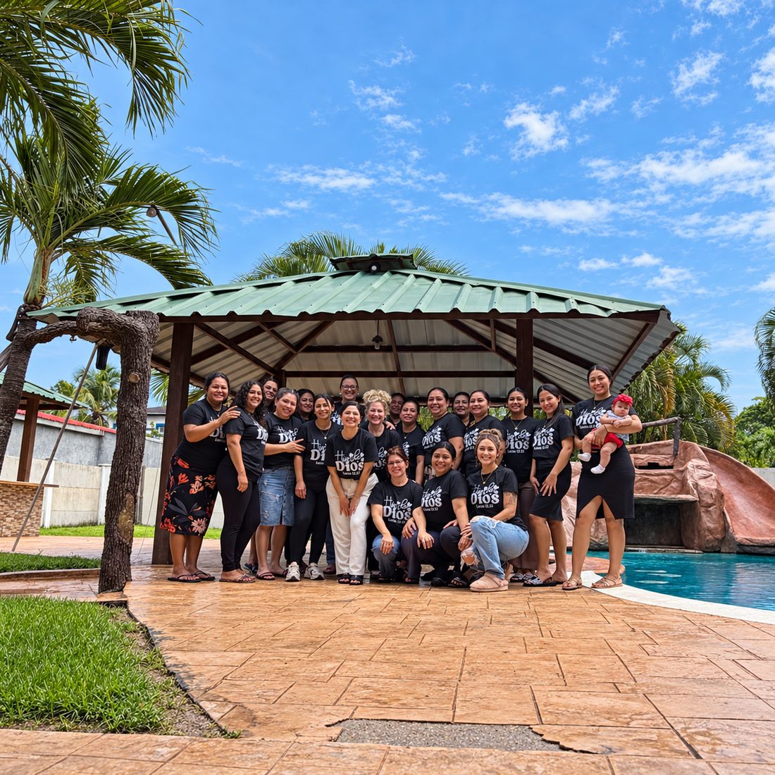 Women in matching Hija de Dios shirts gathered under a pavilion on a mission trip